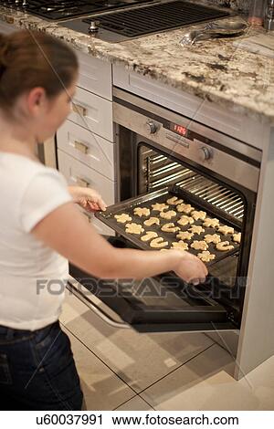 Teenage girl placing baking tray of biscuits in oven View Large Photo Image Stock Image - Teenage girl placing baking tray of biscuits in oven. Fotosearch