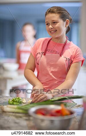 Stock Image - Teenage girl preparing leeks in kitchen. Fotosearch