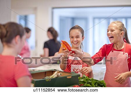 Picture - Teenage girls holding up chillies and carrot in kitchen. Fotosearch