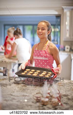 Stock Image - Teenage girls preparing biscuits in kitchen. Fotosearch