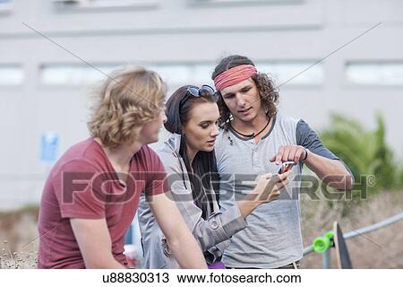 Three young adult friends looking at smartphone on city street View Large Photo Image Stock Image - Three young adult friends looking at smartphone on city street. Fotosearch