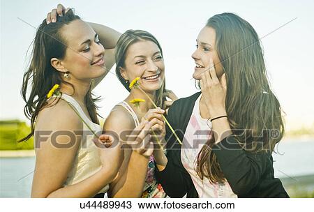 Three young female friends on riverbank holding dandelions View Large Photo Image Stock Image - Three young female friends on riverbank holding dandelions. Fotosearch