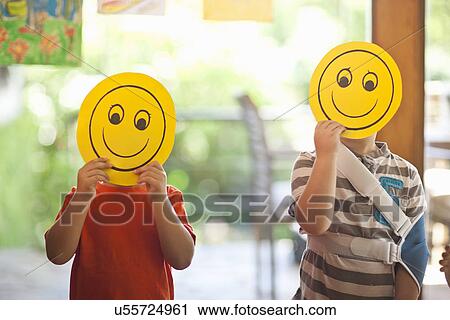 Two boys holding up smiley face masks at nursery school View Large Photo Image Stock Image - Two boys holding up smiley face masks at nursery school. Fotosearch