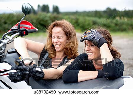 Stock Image - Two female motorcyclists leaning on motorcycle. Fotosearch