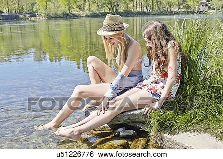 Stock Photograph - Two friends sitting on rocks by water. Fotosearch