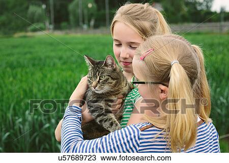 Stock Image - Two sisters in field with domestic cat. Fotosearch