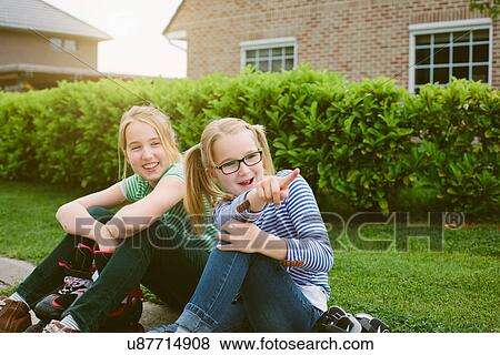 Stock Photo - Two sisters sitting and pointing from sidewalk. Fotosearch