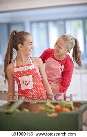 Stock Photograph - Two teenage girls preparing vegetables in kitchen. Fotosearch