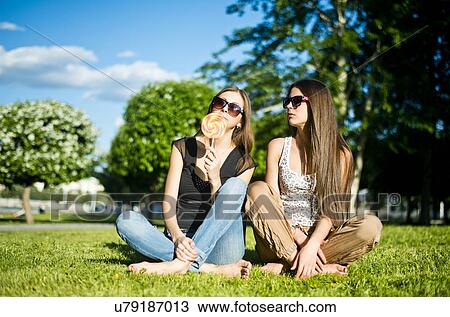 Two young female friends in park, one licking lollipop View Large Photo Image Stock Image - Two young female friends in park, one licking lollipop. Fotosearch