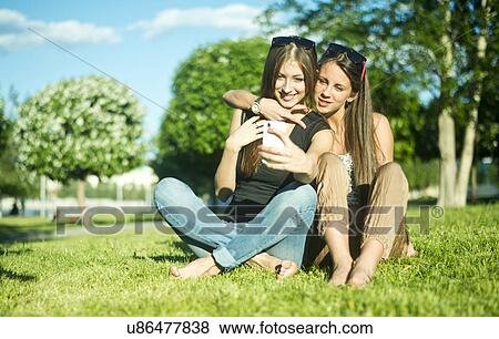 Stock Photo - Two young female friends taking self portrait on smartphone in park. Fotosearch