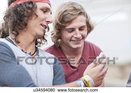 Two young male adult friends looking at smartphone View Large Photo Image Stock Image - Two young male adult friends looking at smartphone. Fotosearch