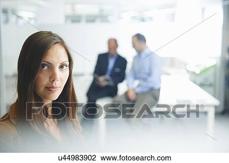 Stock Image - Woman posing for camera, businessmen in background. Fotosearch