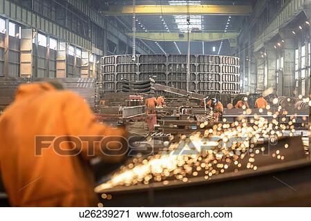 Stock Image - Worker grinding metal construction in marine fabrication factory. Fotosearch