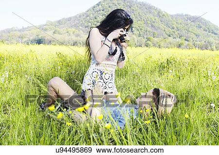 Young couple in field, woman photographing man View Large Photo Image Stock Photo - Young couple in field, woman photographing man. Fotosearch