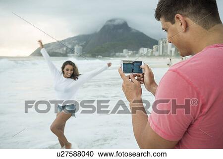 Stock Image - Young couple photographing with smartphone on Ipanema Beach, Rio de Janeiro, Brazil. Fotosearch