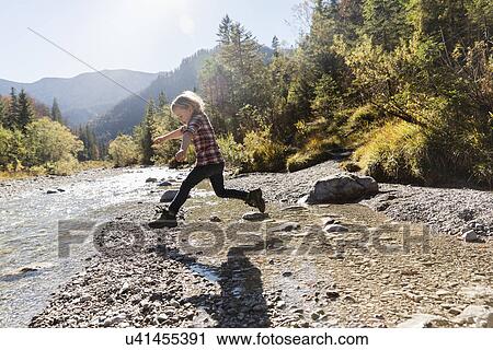 Stock Image - Young girl jumping mid air at riverside. Fotosearch