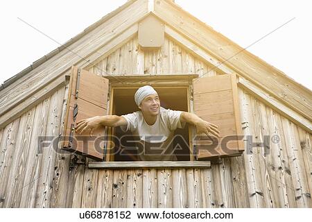 Stock Image - Young male baker leaning opening window shutters. Fotosearch