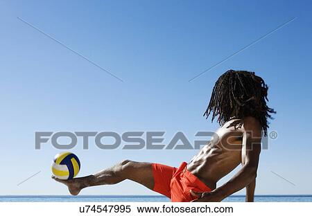 Stock Photography - Young man balancing football on foot at coast. Fotosearch