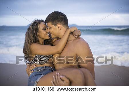Stock Photo - Young man carrying girlfriend in arms on Ipanema Beach, Rio de Janeiro, Brazil. Fotosearch