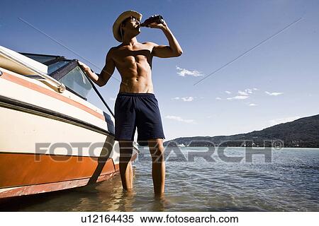 Young man next to power boat drinking from beer bottle, Verbania, Italy View Large Photo Image Stock Photography - Young man next to power boat drinking from beer bottle, Verbania, Italy. Fotosearch