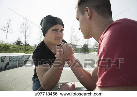Stock Photograph - Young men arm-wrestling in skatepark. Fotosearch