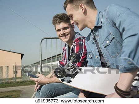 Young men in skatepark, using smartphone View Large Photo Image Stock Image - Young men in skatepark, using smartphone. Fotosearch