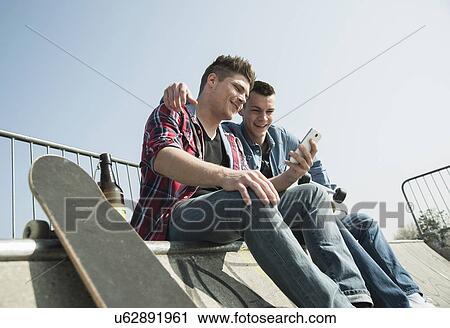 Young men in skatepark, using smartphone, drinking bottle of beer View Large Photo Image Stock Image - Young men in skatepark, using smartphone, drinking bottle of beer. Fotosearch