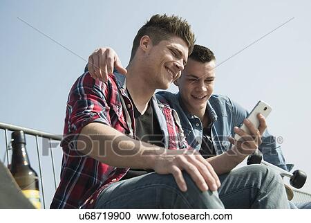Young men in skatepark, using smartphone, drinking bottle of beer View Large Photo Image Stock Image - Young men in skatepark, using smartphone, drinking bottle of beer. Fotosearch
