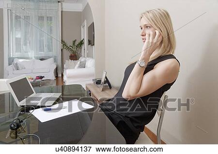 Stock Photo - Young woman chatting on smartphone at home desk. Fotosearch