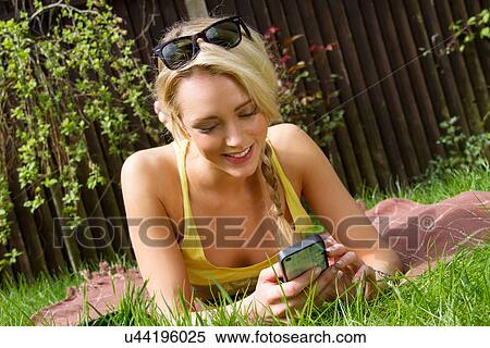 Young woman lying in garden reading texts on smartphone View Large Photo Image Stock Photography - Young woman lying in garden reading texts on smartphone. Fotosearch