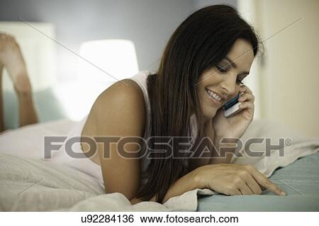 Young woman lying on bed chatting on smartphone View Large Photo Image Stock Photograph - Young woman lying on bed chatting on smartphone. Fotosearch