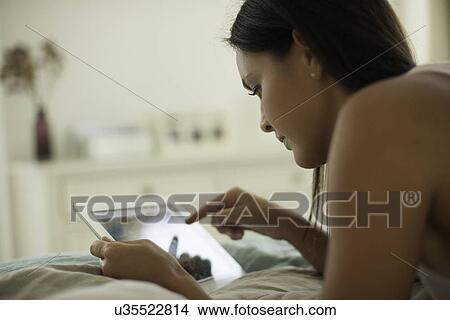 Picture - Young woman lying on bed using digital tablet. Fotosearch