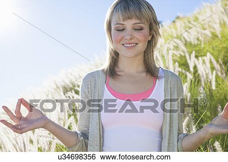 Young woman meditating with eyes closed in long grass View Large Photo Image Stock Photograph - Young woman meditating with eyes closed in long grass. Fotosearch