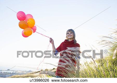 Young woman on grassy hill holding bunch of balloons View Large Photo Image Stock Photograph - Young woman on grassy hill holding bunch of balloons. Fotosearch