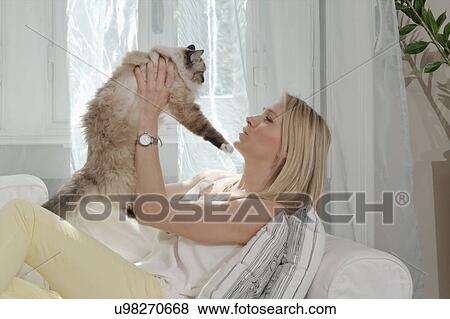 Young woman on sofa holding up cat View Large Photo Image Stock Photo - Young woman on sofa holding up cat. Fotosearch