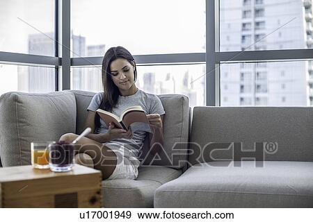 Stock Photo - Young woman on sofa reading book. Fotosearch