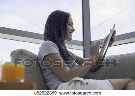 Stock Photo - Young woman on sofa using digital tablet. Fotosearch