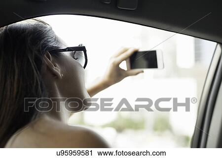 Young woman photographing with smartphone from taxi window View Large Photo Image Stock Image - Young woman photographing with smartphone from taxi window. Fotosearch