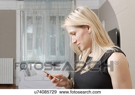 Young woman reading text message on smartphone in dining room View Large Photo Image Stock Photo - Young woman reading text message on smartphone in dining room. Fotosearch