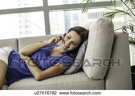 Young woman reclining on sofa chatting on smartphone View Large Photo Image Stock Image - Young woman reclining on sofa chatting on smartphone. Fotosearch