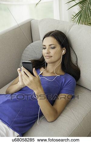 Young woman reclining on sofa listening to music on smartphone View Large Photo Image Stock Photography - Young woman reclining on sofa listening to music on smartphone. Fotosearch