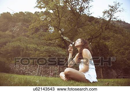 Young woman sitting cross legged in field blowing bubbles View Large Photo Image Stock Image - Young woman sitting cross legged in field blowing bubbles. Fotosearch