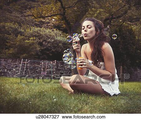 Young woman sitting in field blowing bubbles View Large Photo Image Stock Photo - Young woman sitting in field blowing bubbles. Fotosearch