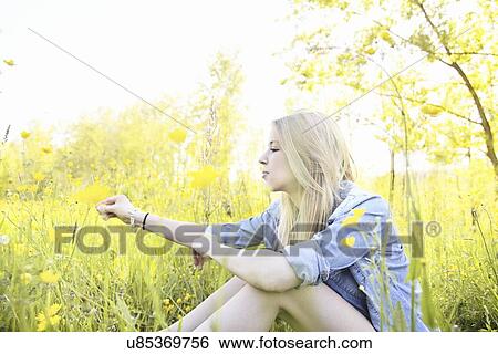 Stock Photograph - Young woman sitting in field with wildflowers. Fotosearch