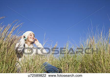 Young woman sitting in long grass listening to headphones View Large Photo Image Stock Image - Young woman sitting in long grass listening to headphones. Fotosearch