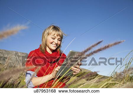 Young woman sitting in long grass using touch screen on digital tablet View Large Photo Image Stock Photo - Young woman sitting in long grass using touch screen on digital tablet. Fotosearch