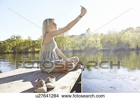 Young woman sitting on jetty photographing herself View Large Photo Image Picture - Young woman sitting on jetty photographing herself. Fotosearch