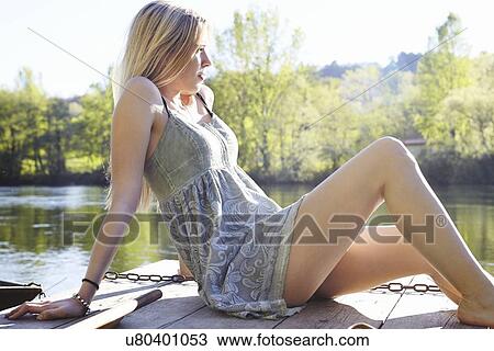 Stock Image - Young woman sitting on jetty. Fotosearch