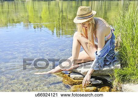 Young woman sitting on rocks by water View Large Photo Image Stock Image - Young woman sitting on rocks by water. Fotosearch