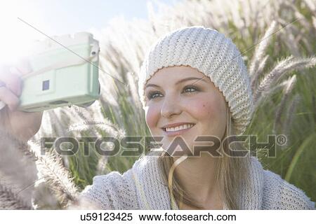 Stock Photography - Young woman taking selfie on digital camera in long grass. Fotosearch